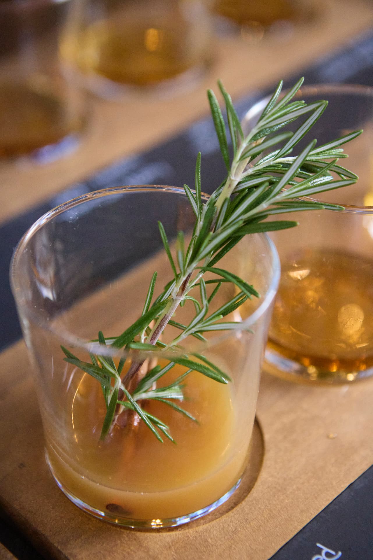 A spiced cider tasting glass garnished with rosemary