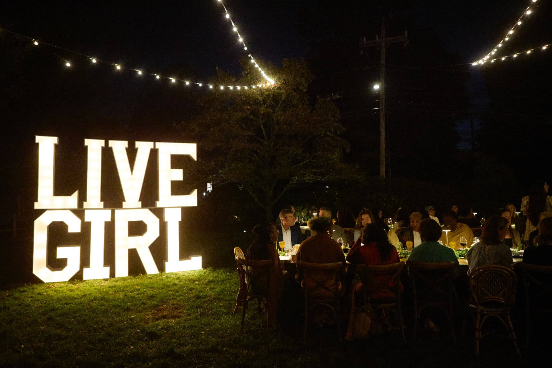The illuminated LiveGirl sign glowing over the candlelit garden dinner